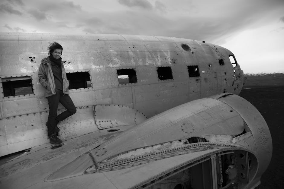 Black and white photo of a traveler leaning on a plane wreck